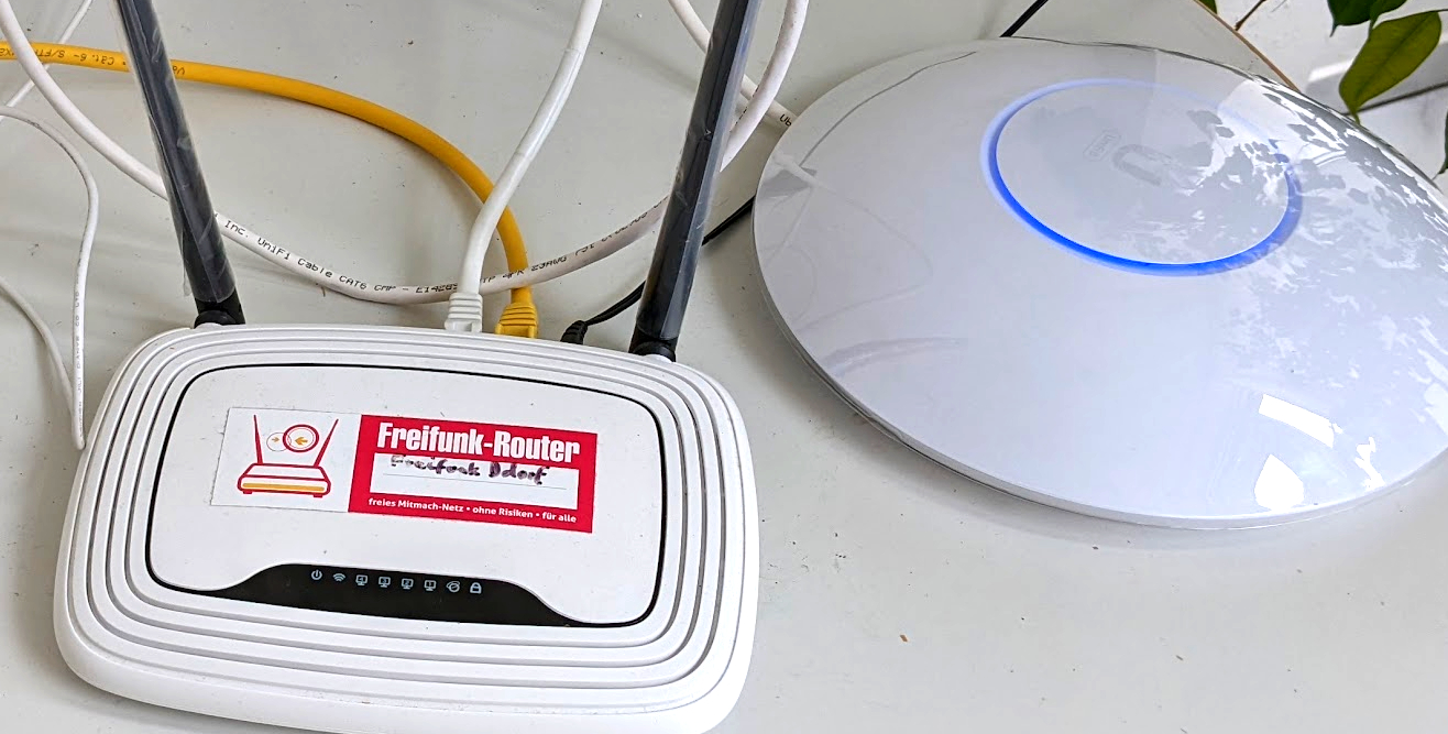 841er Plastikrouter mit Aufkleber “Freifunk-Router” neben einem Unifi Access-Point.